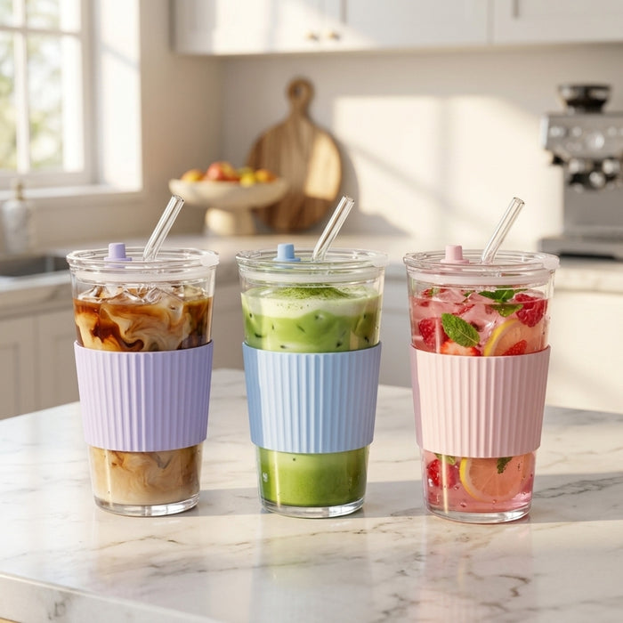 Three clear glass tumblers with ribbed silicone sleeves in lavender, light blue, and pink, each with a clear lid and straw, filled with iced coffee, green drink, and fruit punch on a marble kitchen counter.