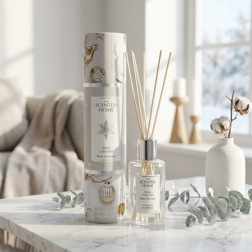 Scented Home Winter Wonderland reed diffuser set on a marble table, featuring a clear glass bottle with natural reeds and its matching cylindrical box with silver and white holiday patterns, styled in a cozy living room setting.